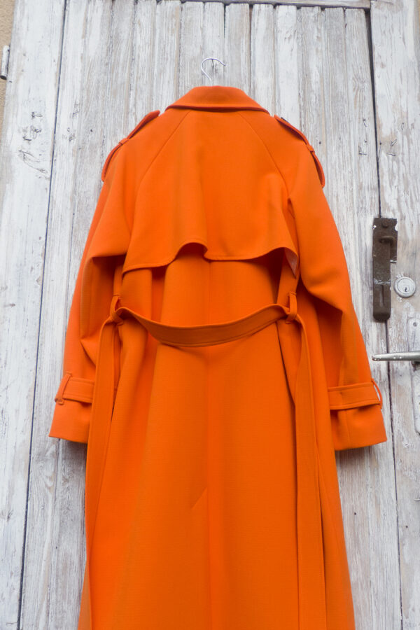 Płaszcz z peleryną na plecach w kolorze pomarańczowym, wiązany w pasie.