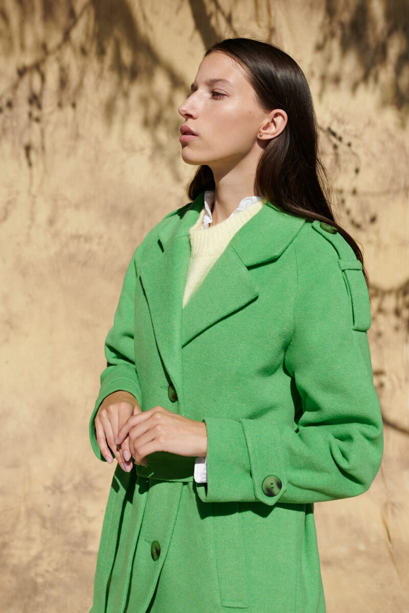 Zielony wełniany płaszcz w stylu trenczu z ozdobnymi pagonami na ramionach i mankietach.