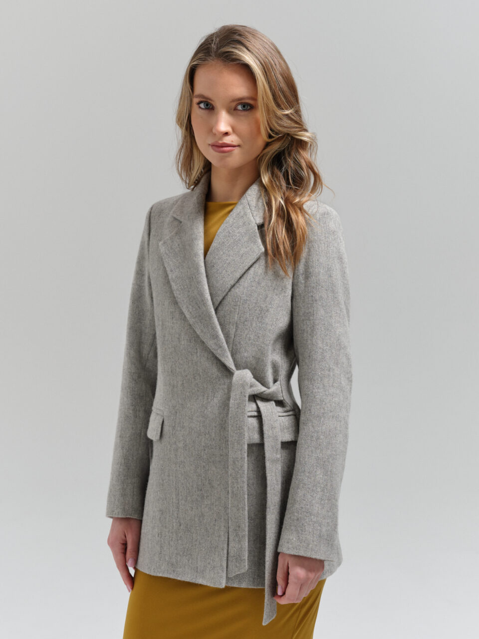 Taliowana marynarka z wysokiej jakości wełny szetlandzkiej. Wiązana finezyjnie z boku. Jasnoszary bazowy kolor.