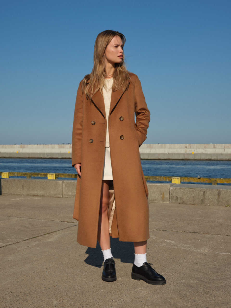 Camelowy, długi płaszcz zimowy o szlafrokowym kroju. Uszyty ze szlachetnej tkaniny wełnianej. Dopieszczony w każdym detalu. Zachwyca miękkością i jakością.