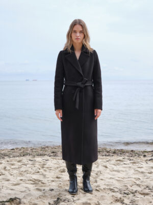 Czarny dopasowany długi płaszcz zimowy, dodatkowo ocieplany. Wiązany i zapinany na guziki. Kołnierz wykładany typu rewers. Klasyczny, ponadczasowy krój. Rzemiślnicza perełka, która posłuży na lata i nada wyrafinowany charakter każdej stylizacji.