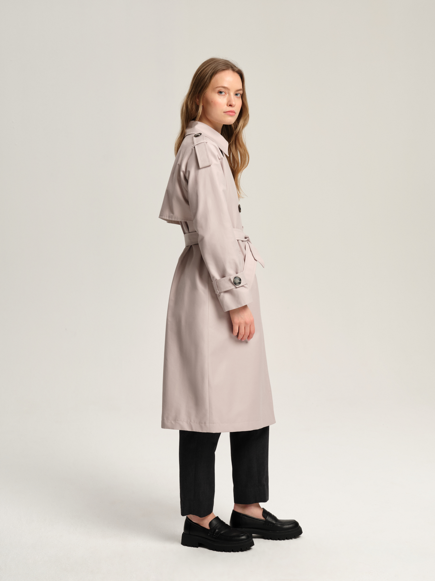 Długi luźny trencz damski w stylu oversize z raglanowymi rękawami wykończonymi ozdobnymi pagonami. Zapinany dwurzędowo na guziki i wiązany w pasie. Ozdobna peleryna na tyle.