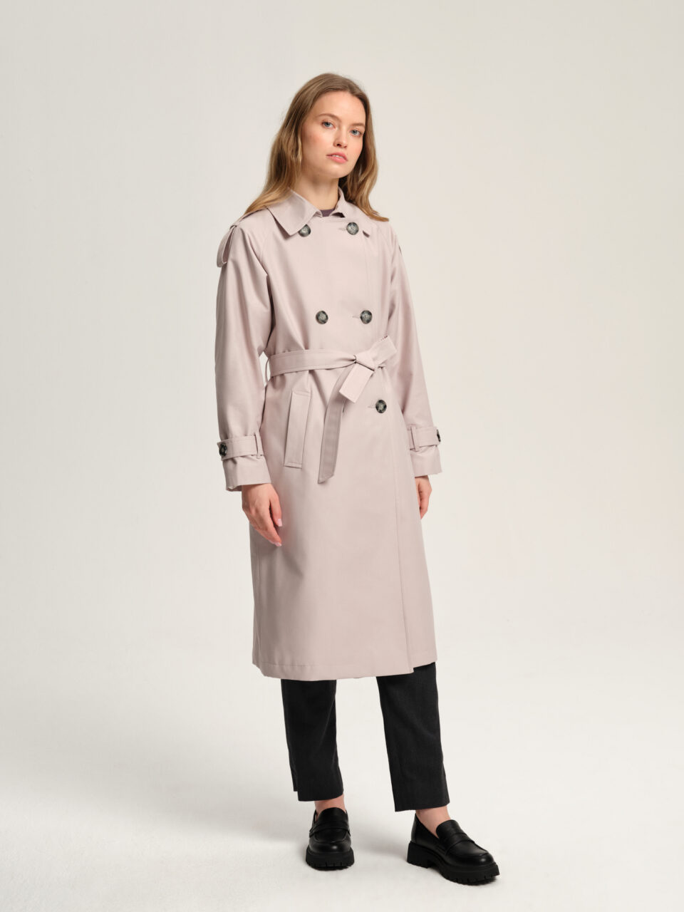 Długi luźny trencz damski z raglanowymi rękawami wykończonymi ozdobnymi patkami. Zapinany na dwa rzędy guzików. Pasek do podkreślenia talii. Idealny do stylizacji wielowarstwowych. Uszyty z pięknej impregnowanej mieszanki bawełny. Świetny na wiosnę i jesień.