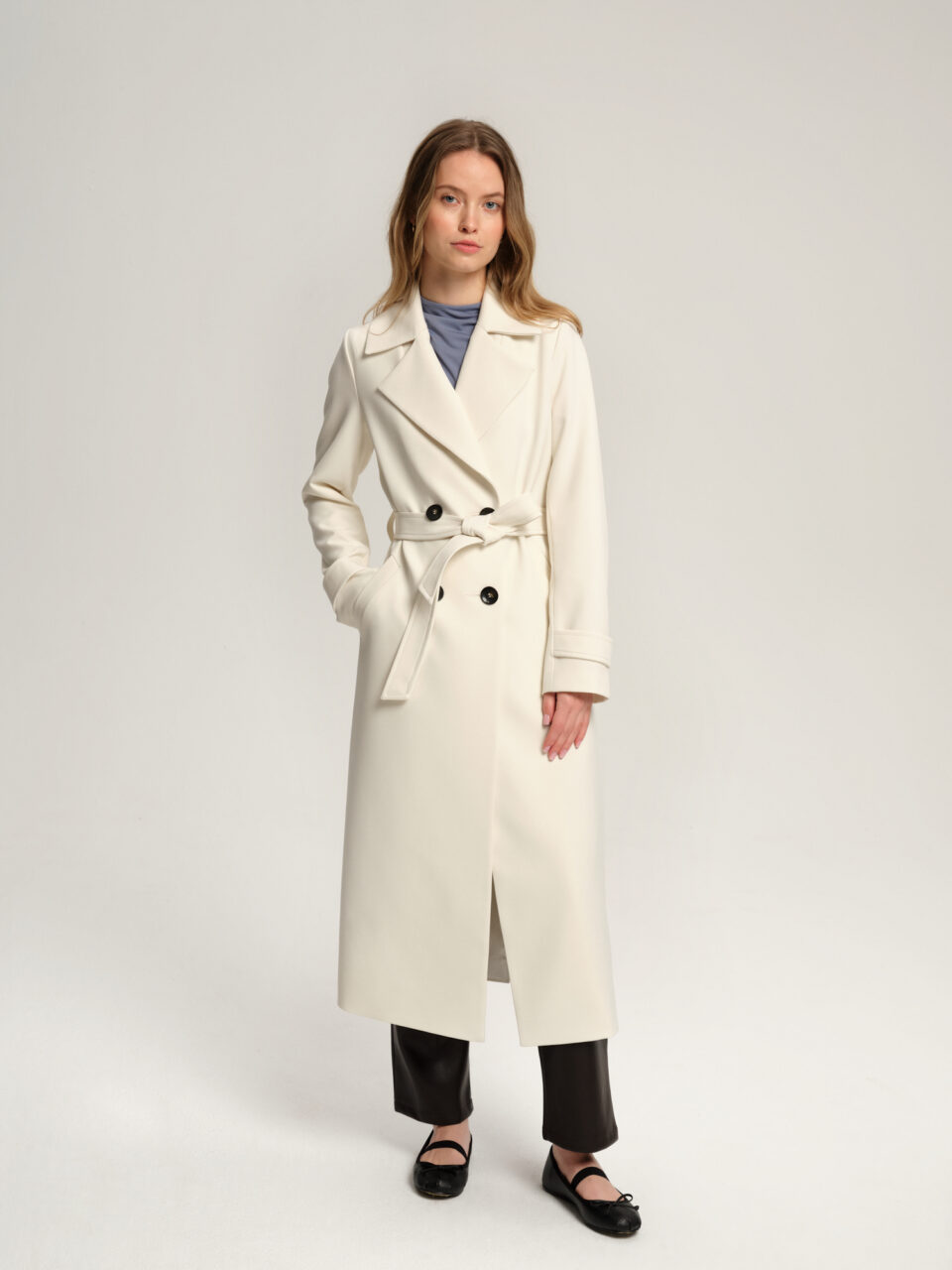 Długi trencz damski w minimalistycznym stylu. Krój szlafrokowy, wygodny. Wykładany kołnierz typu rewers. Zapięcie dwurzędowe na guziki. Dodatkowo wiązany w pasie. Idealny na przejściowe pory roku.