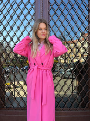 Długi, dwurzędowy prochowiec wiosenny w delkiatnie oversizowym stylu z rękawem raglanowym. Wiązany w pasie i zapiany na kontrastowe guziki.