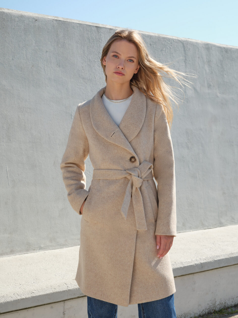 Jednorzędowy płaszcz wełniany o asymetrycznym przodzie. Zapinany na ręcznie przyszywane guziki. Szykowny szalowy kołnierz tworzący stójkę. Uszyty z wełny dziewiczej w beżową jodełkę.