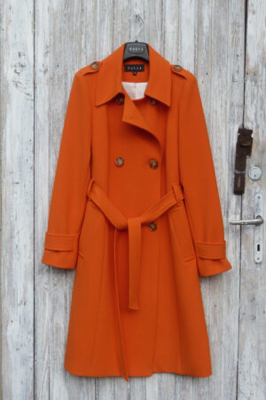 Klasyczny trencz dwurzędowy dopasowany, wiązany w pasie, w kolorze pomarańczowym.