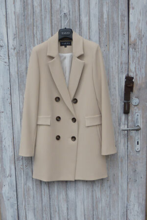 Krótki trencz luźny bez paska z dwurzędowym zapięciem w kolorze beżowym.