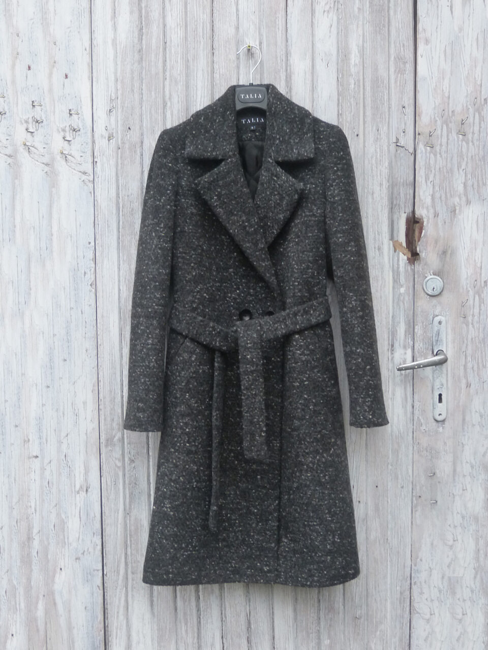 Melanżowy wełniany płaszcz zimowy z dodatkiem kaszmiru. Klasyczny krój, wiązany w pasie. Dopasowany tył i profilowny przód. Klapy wykończone rewersem.