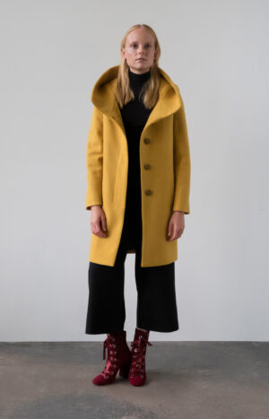 Miodowy płaszcz z kapturem przed kolano. Kryte, jednorzędowe zapięcie na guziki. Prosty krój. Minimalistyczny styl.