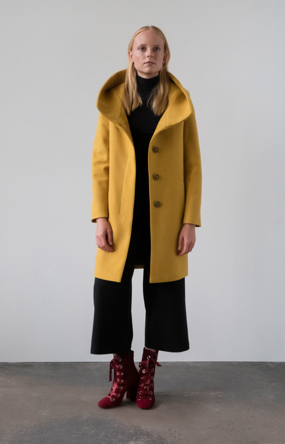 Miodowy płaszcz z kapturem przed kolano. Kryte, jednorzędowe zapięcie na guziki. Prosty krój. Minimalistyczny styl.