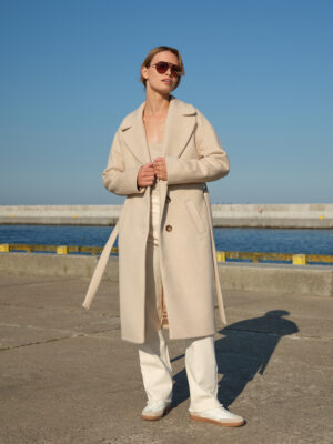 Ocieplany zimowy płaszcz wełniany w beżową jodełkę o luźnym, swobodnym kroju. Zapinany jednorzędowo na guziki i wiązany. Utrzymany w ponadczasowym stylu. Szykowny, ciepły i wygodny.