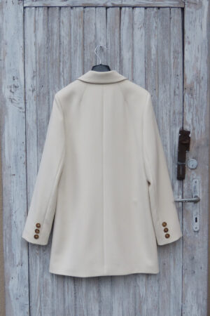 Tył krótkiej kurtki damskiej w kolorze śmietankowym z guzikami na mankietach.