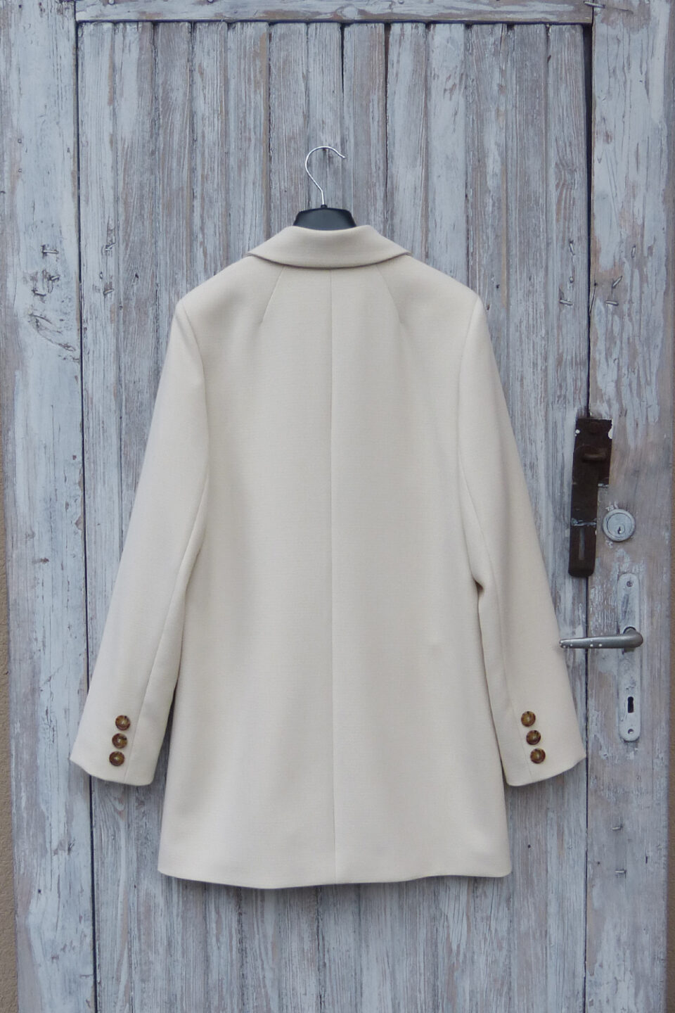 Tył krótkiej kurtki damskiej w kolorze śmietankowym z guzikami na mankietach.