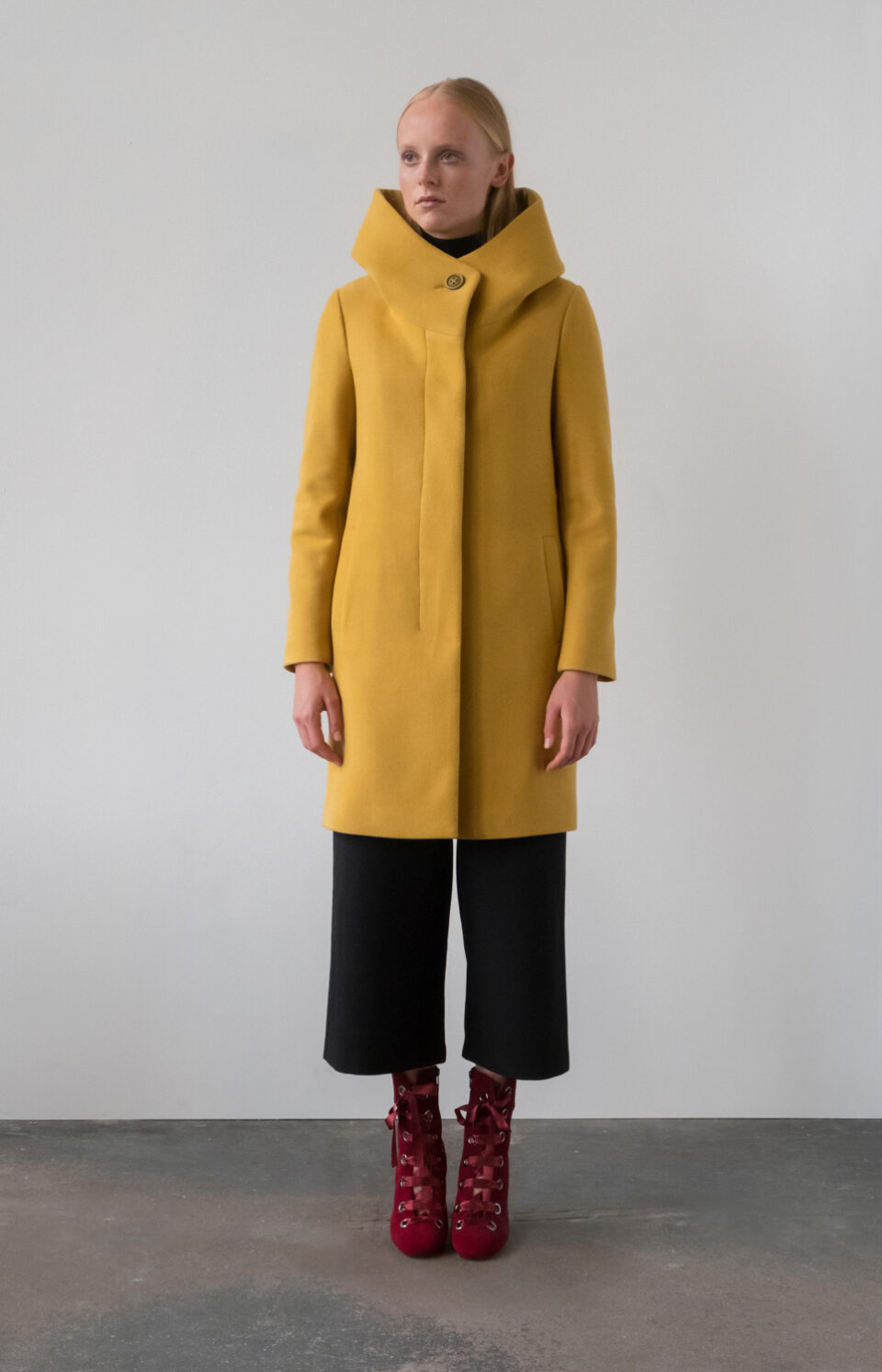 Płaszcz damski z kapturem przed kolano. Jednorzędowy zapinany na guziki. Kryte zapięcie. Ze stójką przekształcającą się w kaptur.