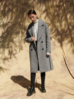 Zimowy płaszcz za kolano, dwurzędowy w czarno-białą jodełkę, zapinany na guziki.