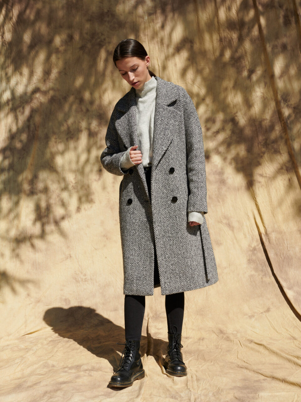 Zimowy płaszcz za kolano, dwurzędowy w czarno-białą jodełkę, zapinany na guziki.