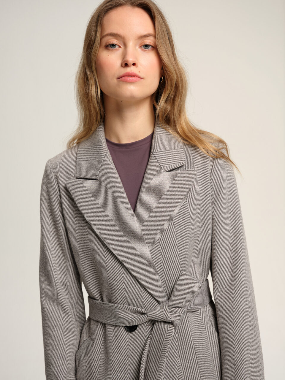 Płaszcz przejściowy w czarno-białą jodełkę. Uszyty z bawełnianej mieszanki i acetatowej podszewki. Idealny na wiosnę i jesień. Materiał i podszewka zapewnią komfort noszenia mimo zmieniającej się pogody. Taliowany. Z paskiem. Klasycznie wszywany rękaw. Kołnierz typu rewers.