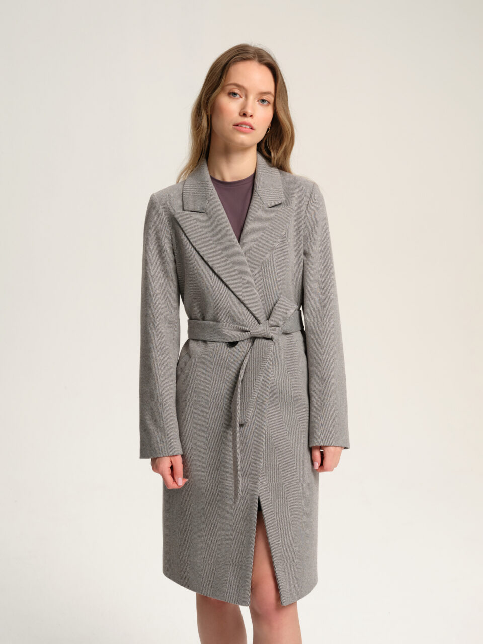 Płaszcz damski z bawełnianej mieszanki w czarno-białą jodełkę. Świetna alternatywa dla prochowca. Taliowany, podkreśla figurę, jednak jej nie przytłacza. Z paskiem. Długość w kolano. Ręcznie szyty.