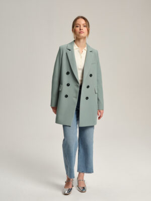 Trencz krótki o kroju marynarki. Luźna, oversizowa forma. Zapinany dwurzędowo na guziki. Klasycznie wszywany rękaw, wykończony ręcznie przyszywanymi guzikami. Długość do połowy uda.