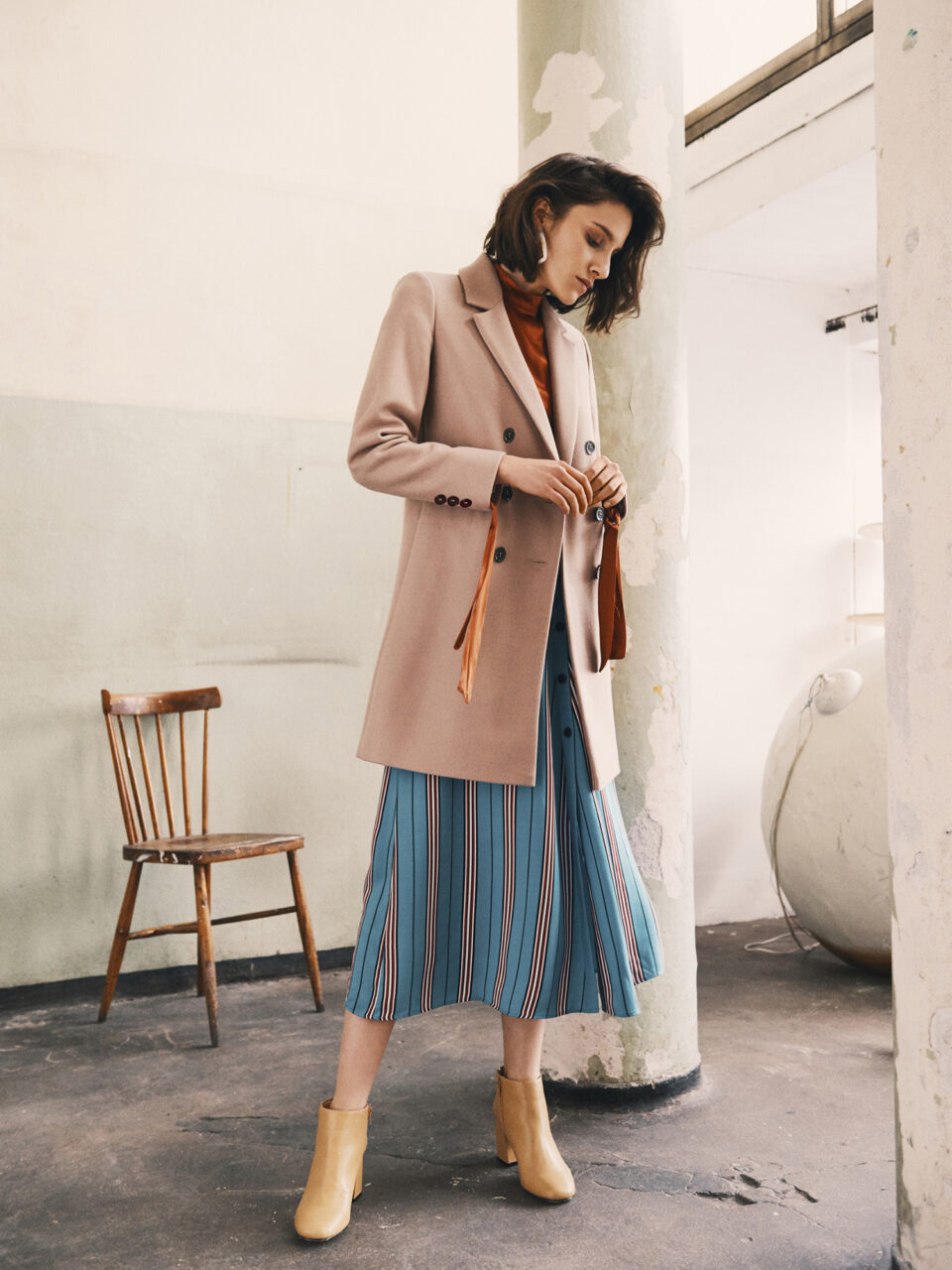 Wiosenny płaszcz damski z kieszeniami w kolorze jasnego kamelu o długości przed kolano.