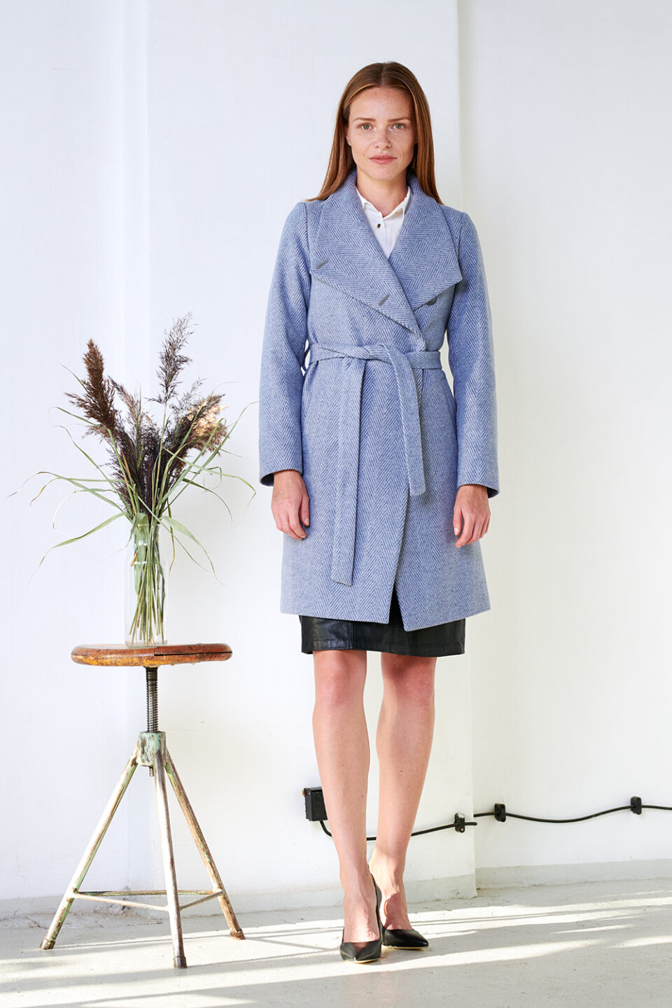 Wysoko zapinany zimowy płaszcz w jodełkę, którego zapięty kołnierz tworzy otulającą stójkę. Wiązany, Pasek w komplecie. Asymetryczny przód.