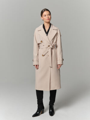 Długi trencz damski w chłodnym kremowym odcieniu. Zapinany dwurzędowo i wiązany. Ozdobne pagony i pasek na rękawach.