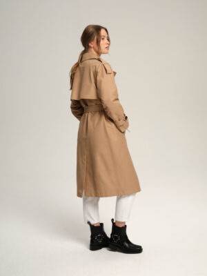Długi beżowy trencz damski oversizowy podpinany wysoko. Dwurzędowy, z peleryną i pagonami. Uszyty z tkaniny bawełnianej pokrytej hydrofobową warstwą.