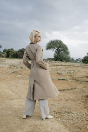 Długi beżowy trencz damski o dopasowanym kroju. Wiązany. Kołnierz rewers.