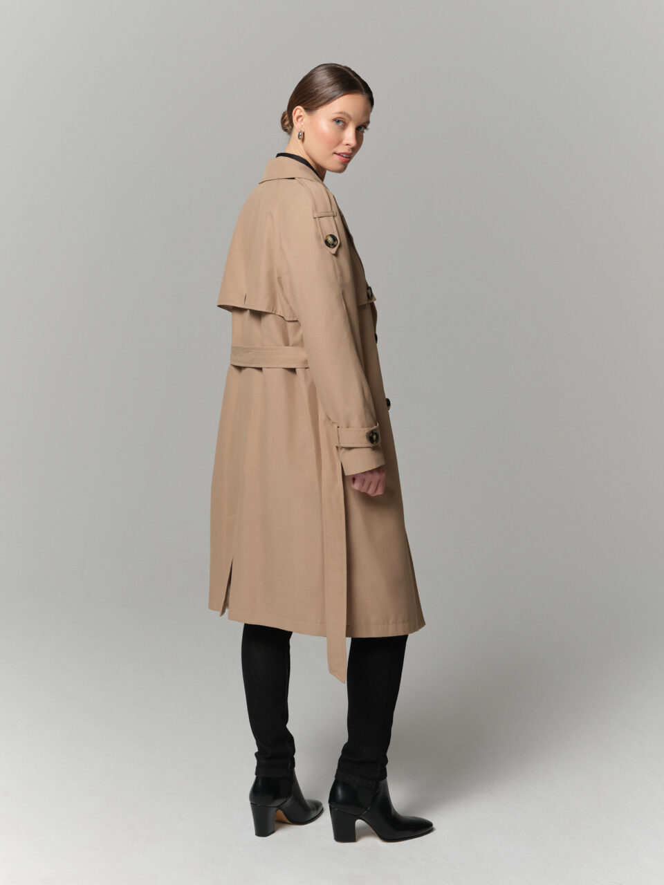 Beżowy trencz damski w luźnym kroju z mieszanki bawełny. Ozdobna peleryna na tyle i przodzie.