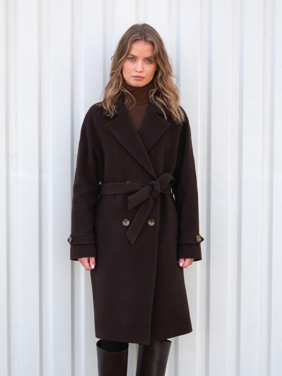 Czekoladowy płaszczyk o długości do kolan. Raglanowy rękaw dodaje luzu i nowoczesności. Wiązany i zapinany na guziki.