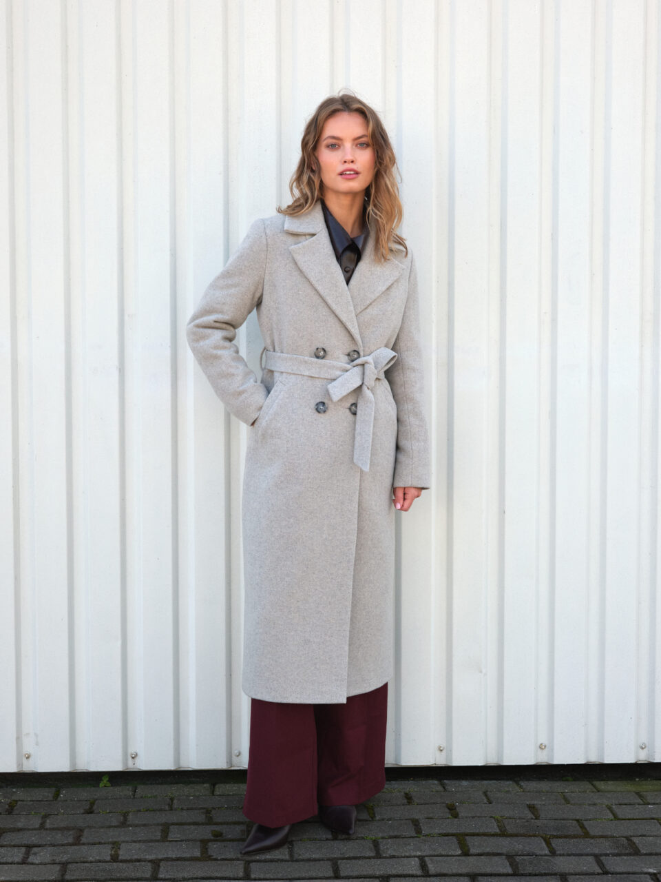 Klasyczny długi płaszcz zimowy w szaro-beżowym melanżowym odcieniu. Wiązany i zapinany dwurzędowo. Dopasowany.