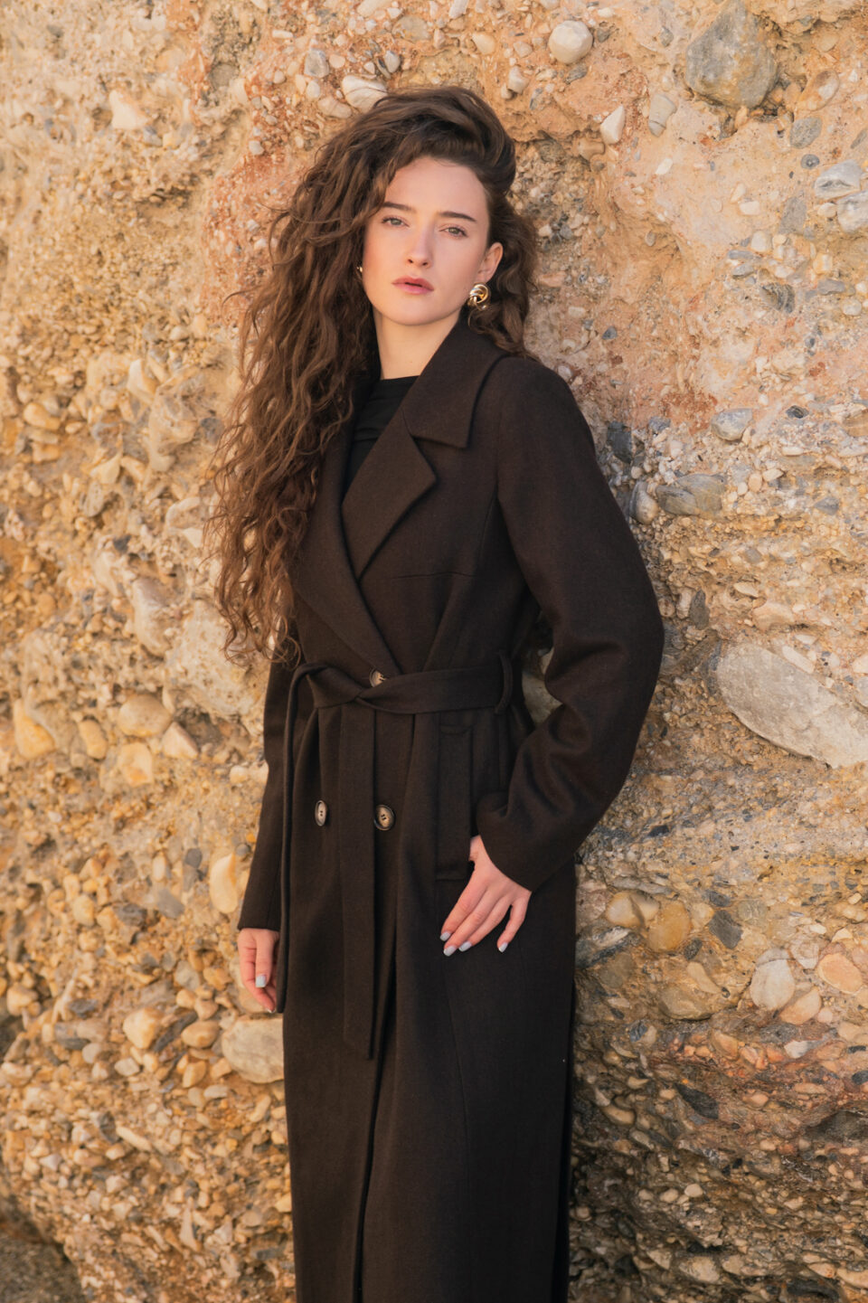 Wełniany płaszcz przejściowy o szlafrokowym kroju. Zapinany na guziki i wiązany. Czekoladowy kolor.