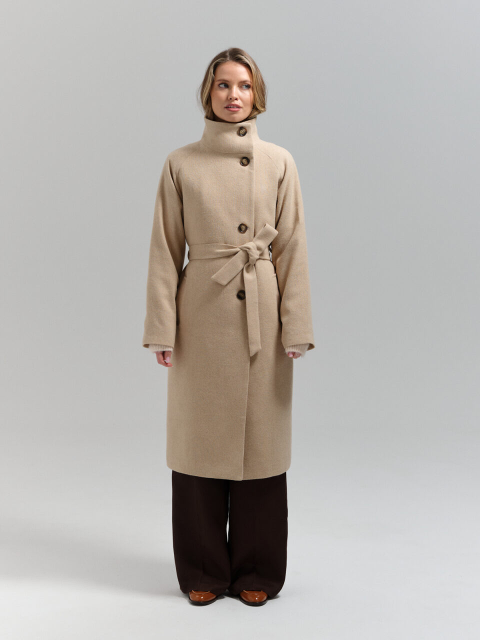 Długi wełniany płaszcz przejściowy ze stojką w ciepłym, beżowym diagonalu. Zapinany asymetrycznie.