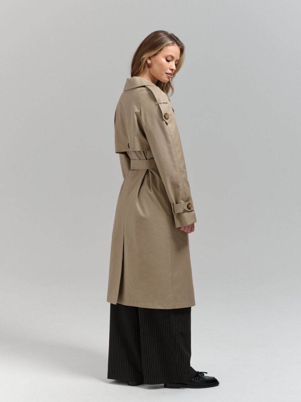 Klasyczny trencz damski o nowoczesnym, swobodnym kroju. Raglanowy rękaw, pagony, peleryna na plecach. Zapinany dwurzędowo. Wiązany.