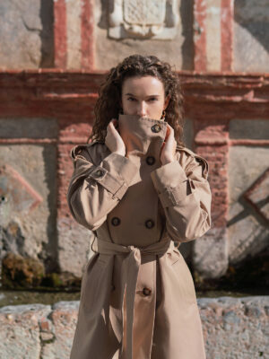 Długi beżowy bawełniany trencz damski w stylu oversize z wysokim kołnierzem.